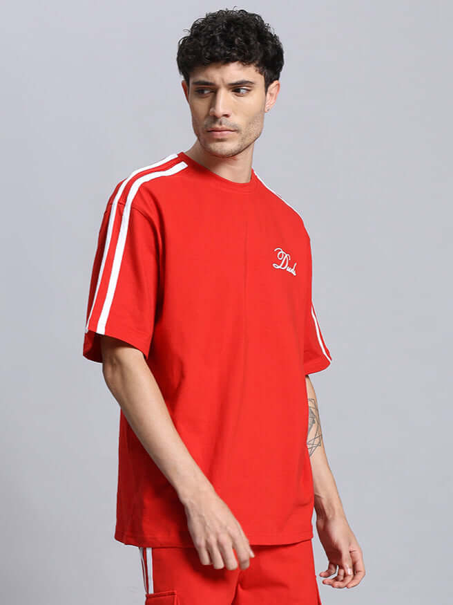 Model wearing SCOTIA OVER-SIZED COTTON T-SHIRT RED, featuring bold minimal design with white stripes on sleeves.
