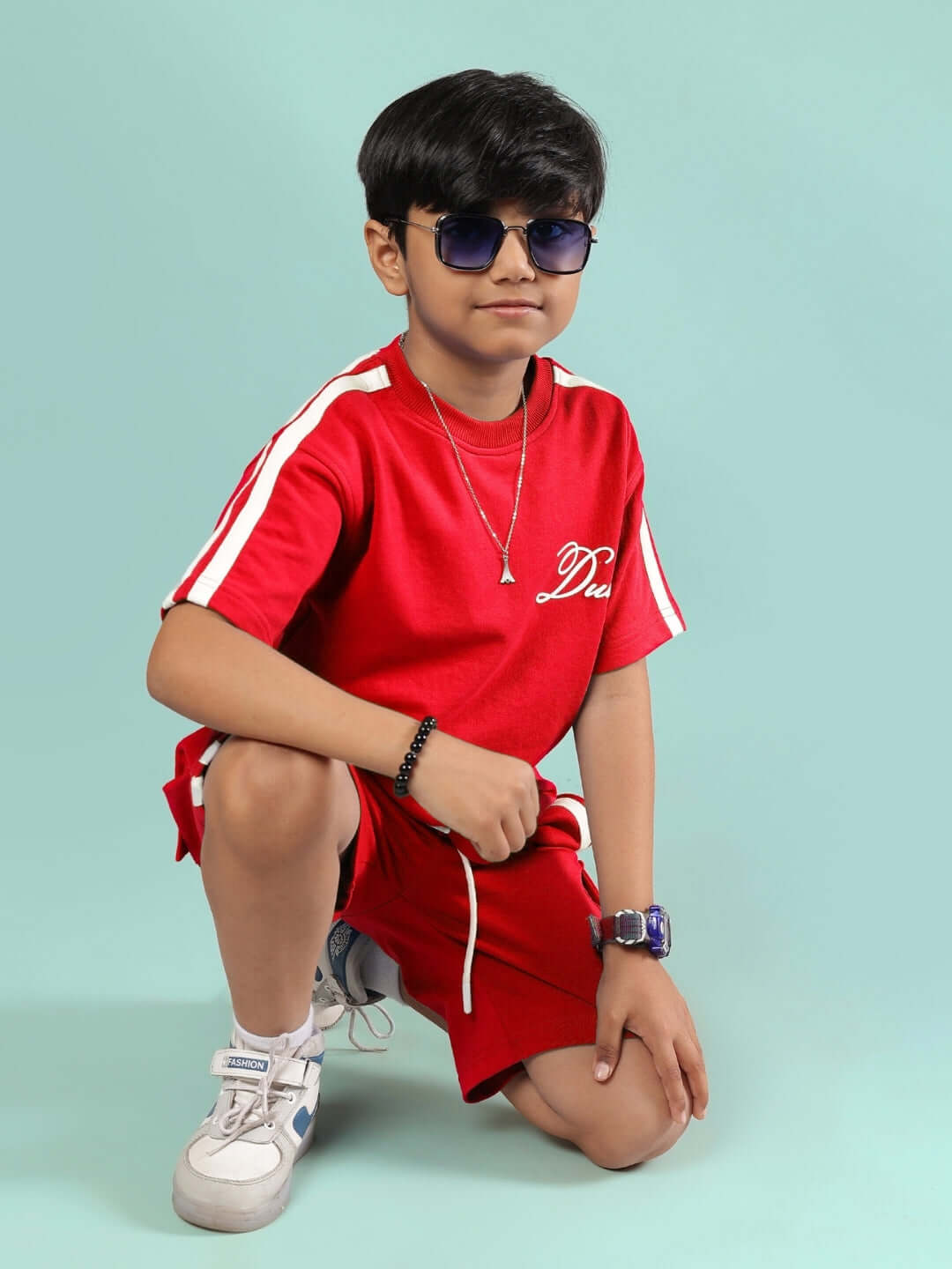 Child wearing Scotia Summer Co-Ord for Boys & Girls Red, sporty red outfit with white stripes, in a stylish pose with sunglasses.