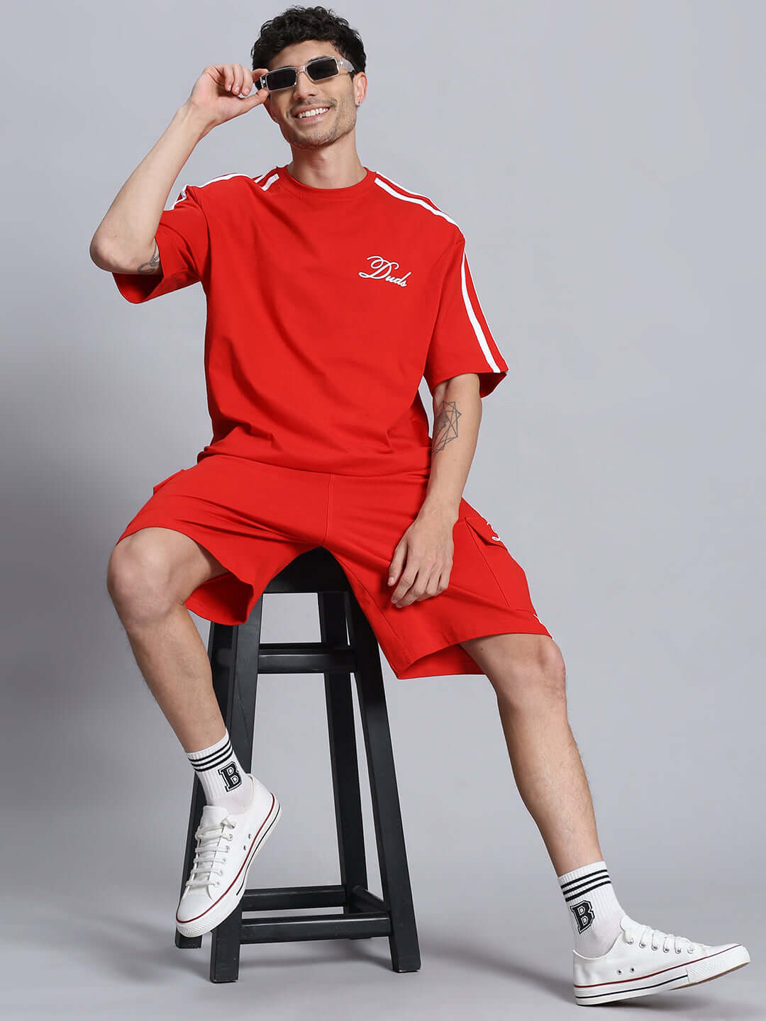 Man wearing red SCOTIA SUMMER CO-ORD SET, sitting on a stool, showcasing premium cotton fabric. Casual summer outfit, sporty style.
