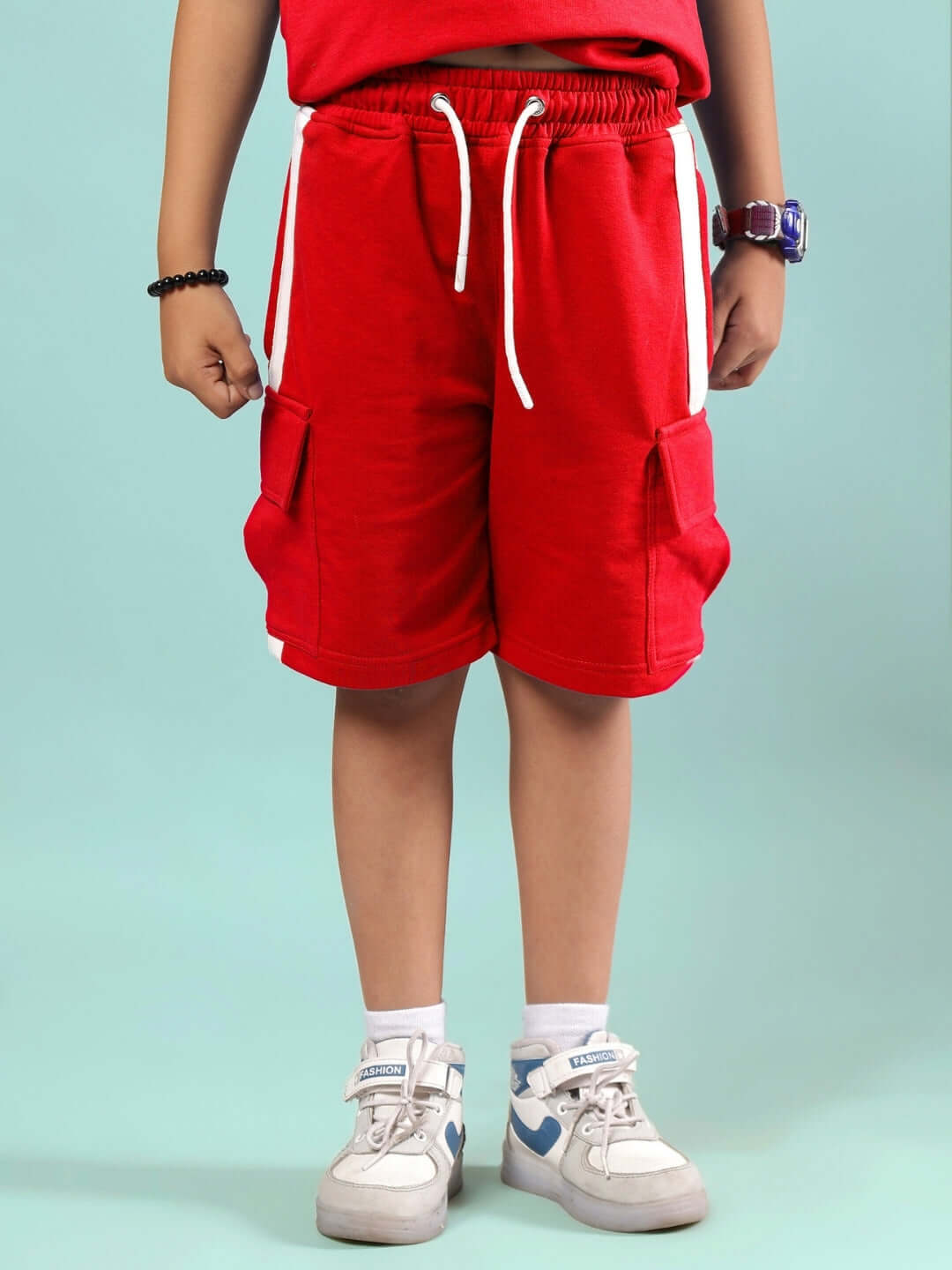Child wearing SCOTIA SUMMER CO-ORD FOR BOYS & GIRLS RED shorts set with sneakers, standing against a blue background.