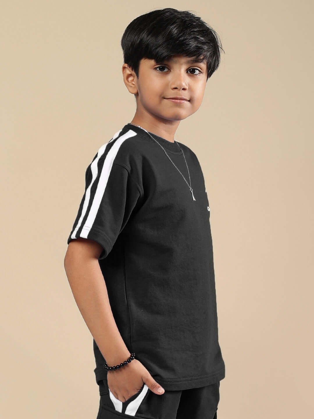 Boy wearing a black SCOTIA T-SHIRT FOR BOYS & GIRLS BLACK with white stripe on sleeve, side view with hands in pockets.
