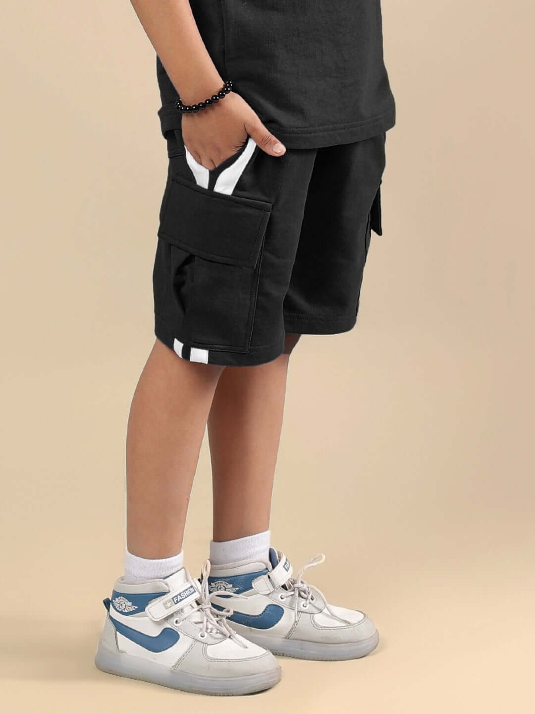 Child wearing SCOTIA SHORTS FOR BOYS & GIRLS BLACK with sneakers, beige background.