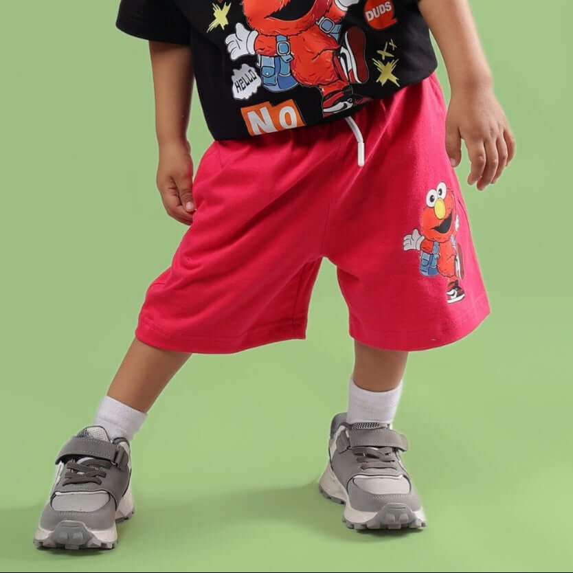 Child wearing SESAME SHORTS FOR BOYS & GIRLS PINK standing against a green background.