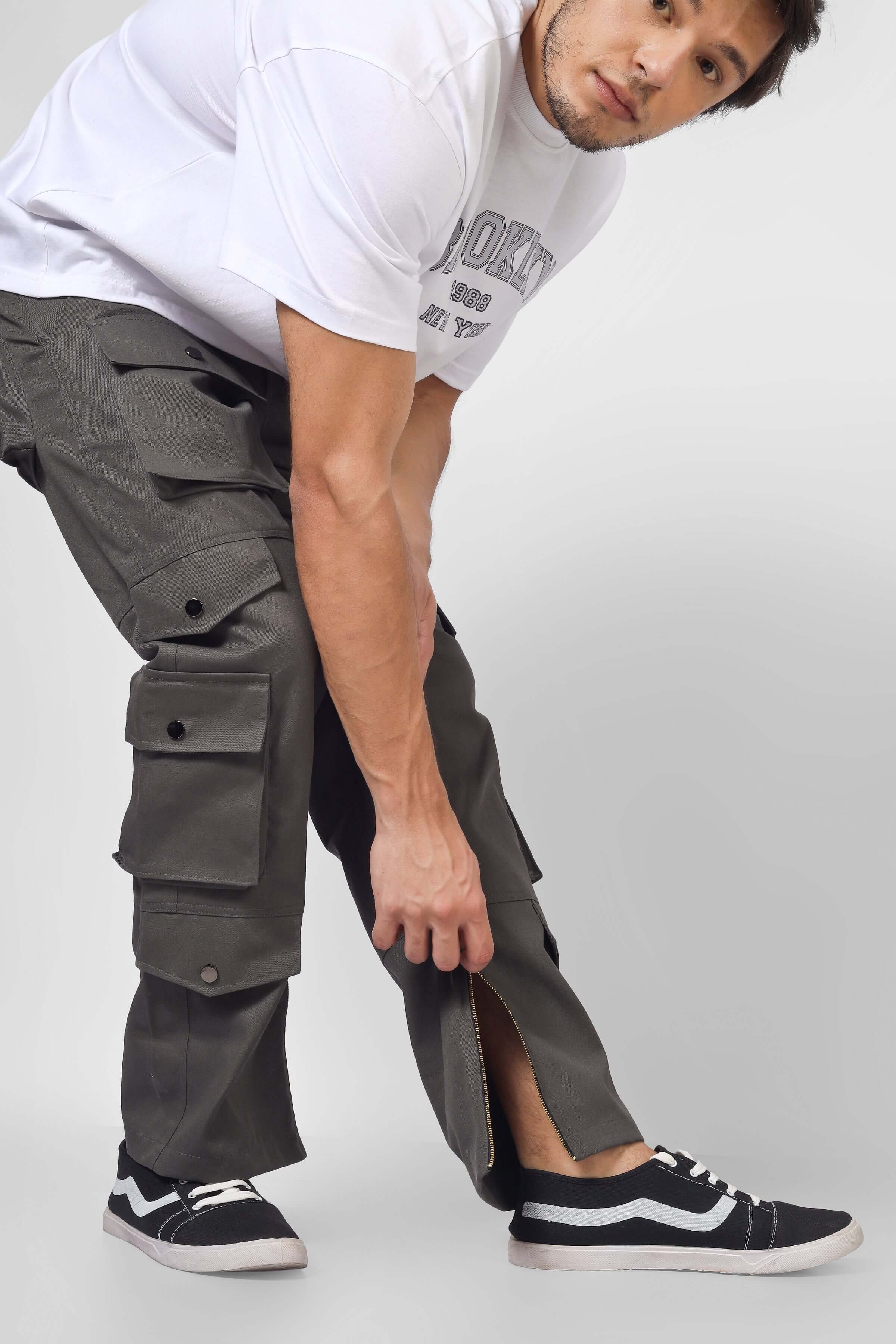 Man wearing shadow grey cargo pants with 8 pockets, adjusting ankle zip. Casual streetwear fashion.