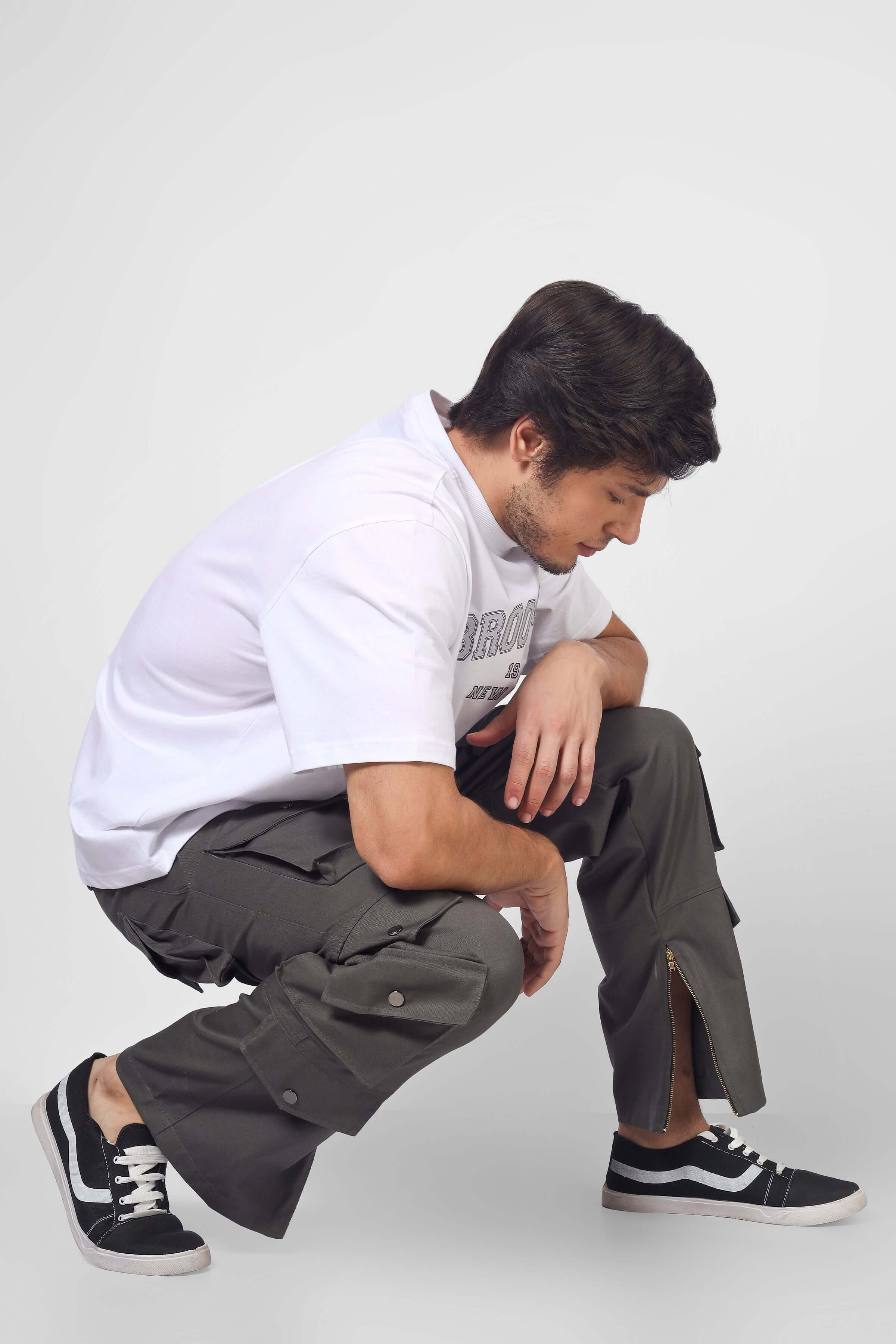 Man wearing shadow grey cargo pants with 8 pockets, crouching in a casual pose, showcasing the pants' utility and style.