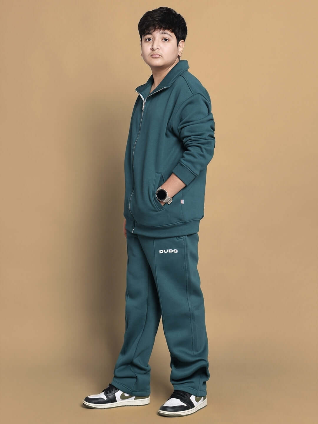 Child wearing teal green shaggy fleece jacket and pants set by DUDS, showcasing a casual look against a beige background.