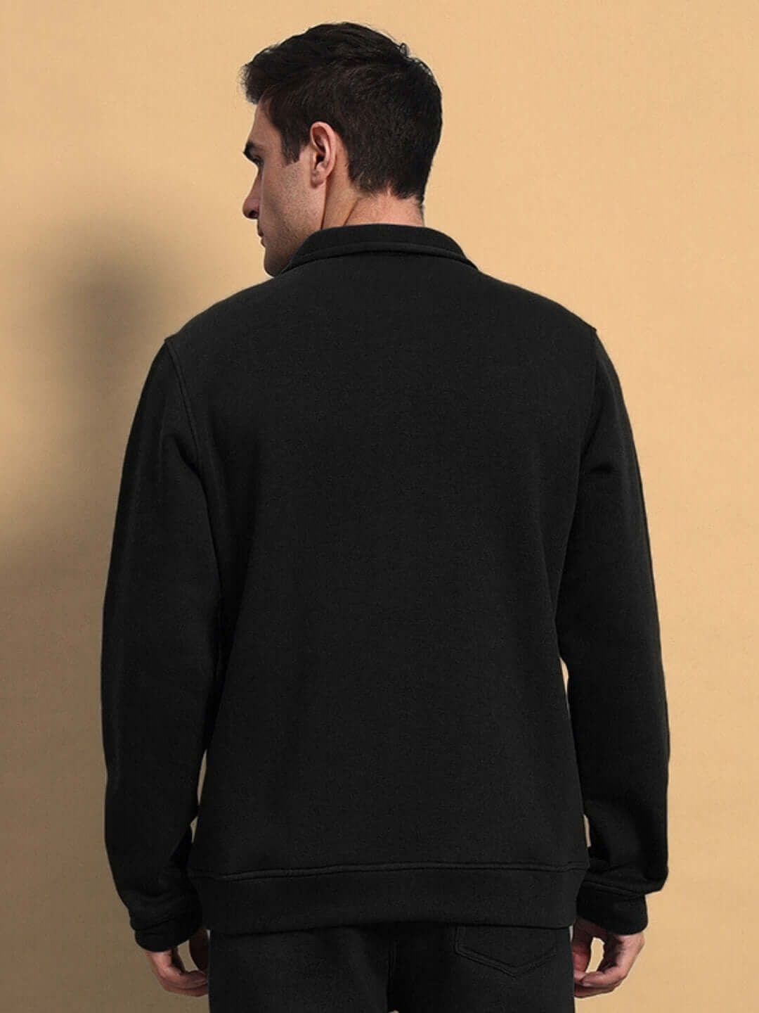 Back view of a black shaggy cotton fleece jacket worn by a model against a beige background.