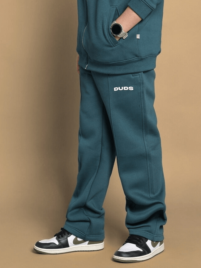 Child wearing teal green shaggy fleece joggers, featuring plush fabric and 'DUDS' logo, styled with sneakers and a watch.