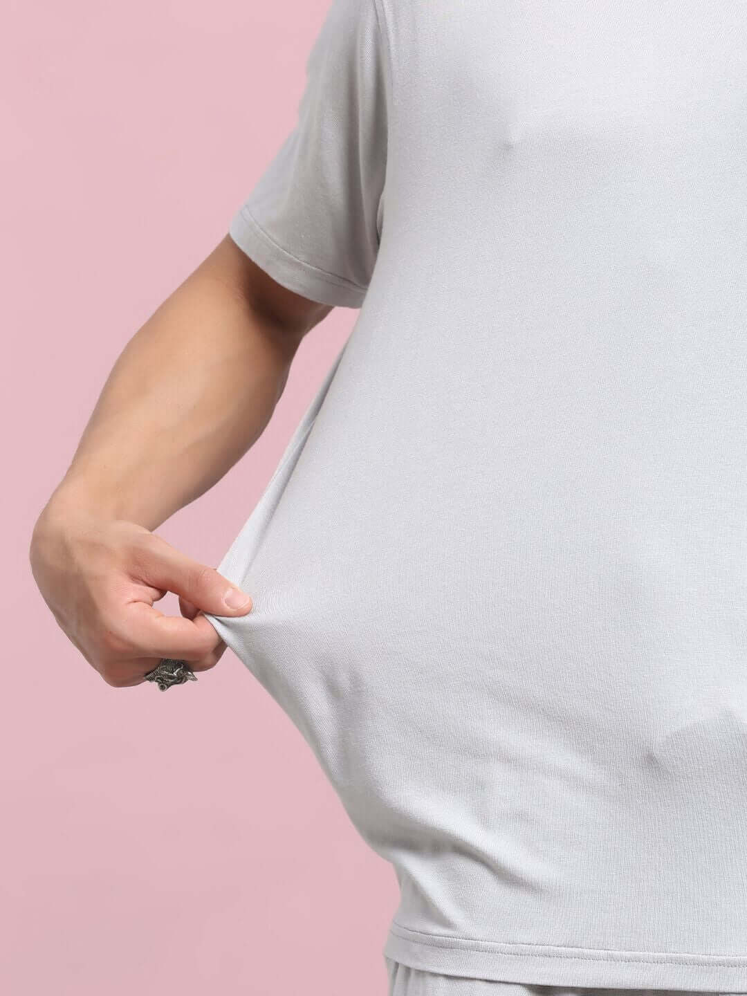 Close-up of model wearing AMBLE grey T-shirt made from premium heavy gauge fabric, demonstrating stretch and texture, against pink background.