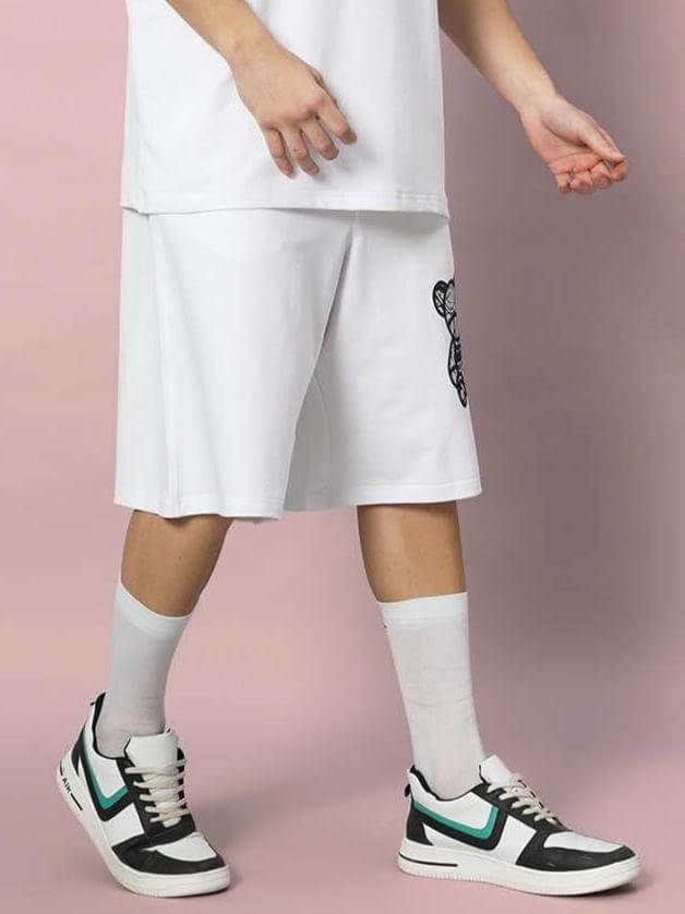 Boy wearing SHIMMY REGULAR FIT SHORTS WHITE with sneakers and socks against pink background