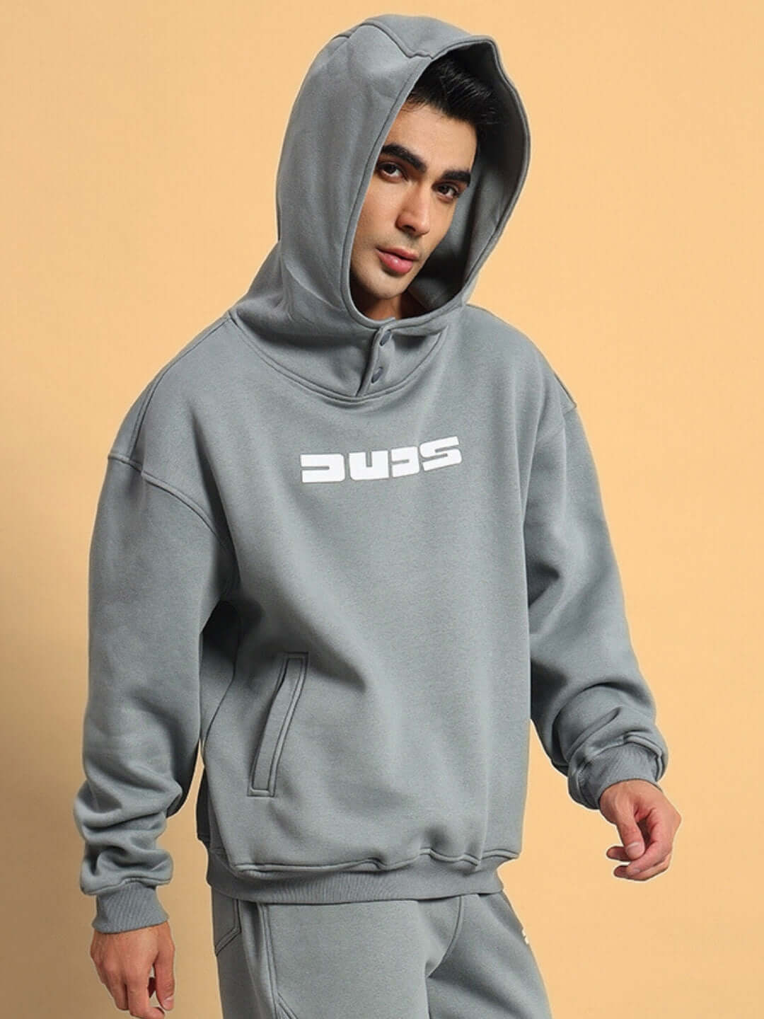 Model wearing gray SHOOTER fleece hoodie by DUDS, showcasing casual style with hood up. Made-to-order, customizable fit available.