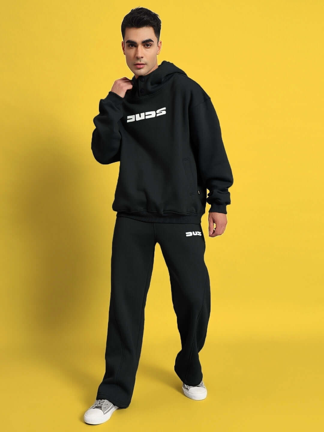 Model wearing WEARDUDS SHOOTER FLEECE CO-ORD BLACK, featuring a hoodie and pants on a yellow background.