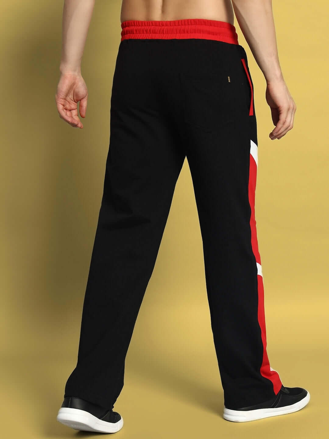 Model wearing black-red Shroud Relaxed Fit Joggers by DUDS, showcasing back view and red side stripes on a yellow background.