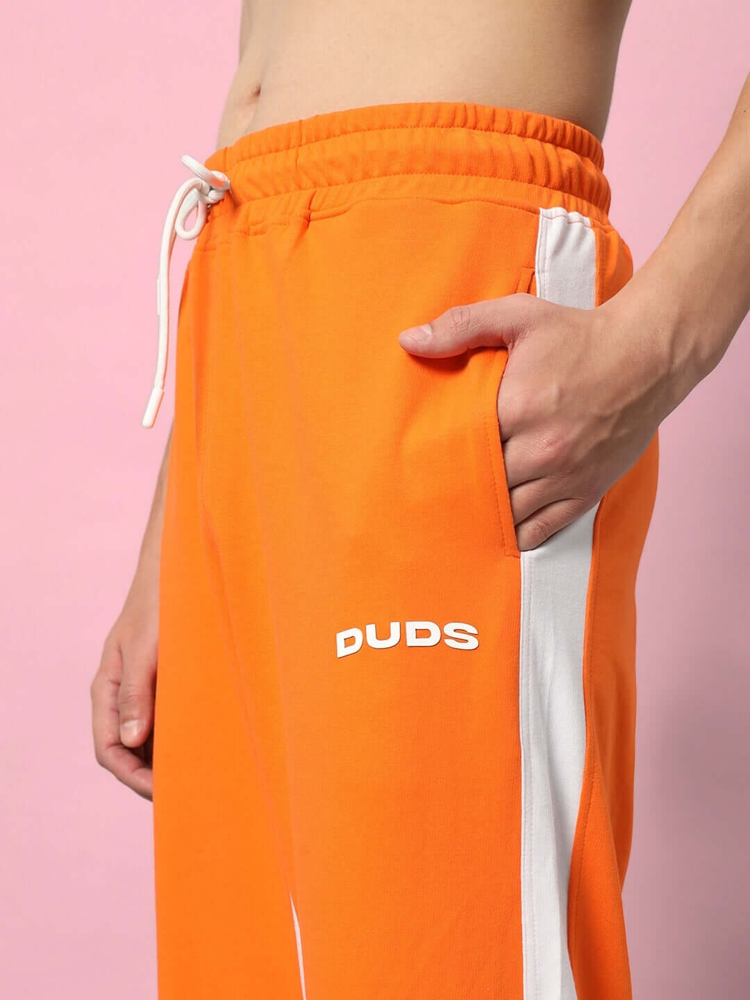 Close-up of orange side seam baggy jogger by DUDS with white stripe detail, showcasing comfortable fit and pocket design.