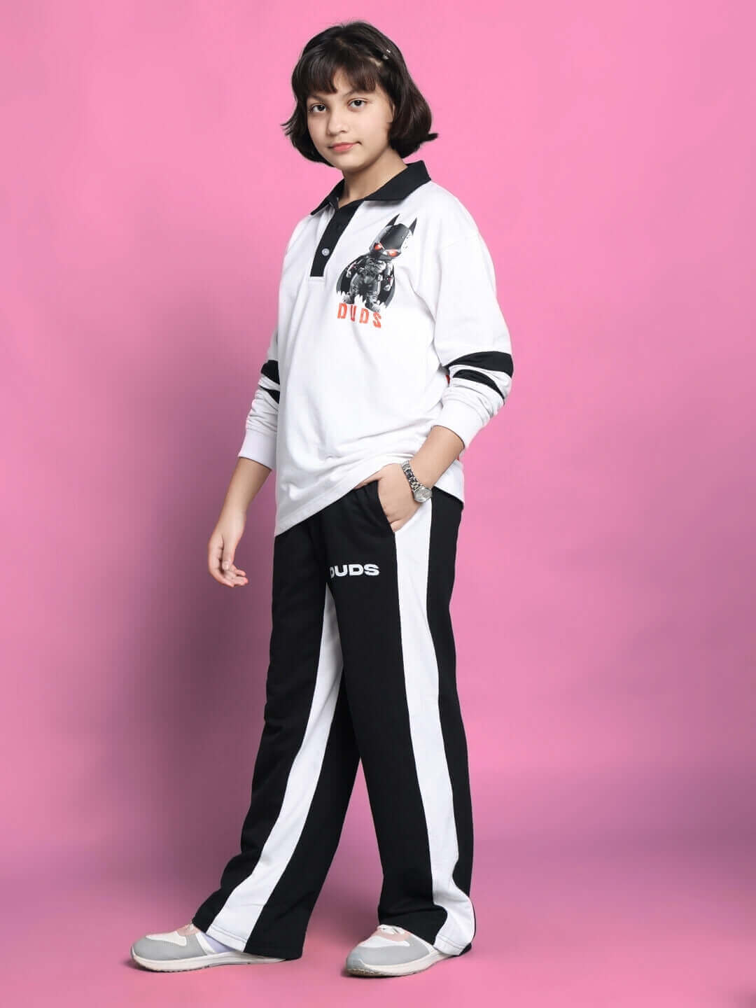 Young person wearing a white Robin oversized sweatshirt for boys and girls, paired with black and white pants, standing against a pink background.
