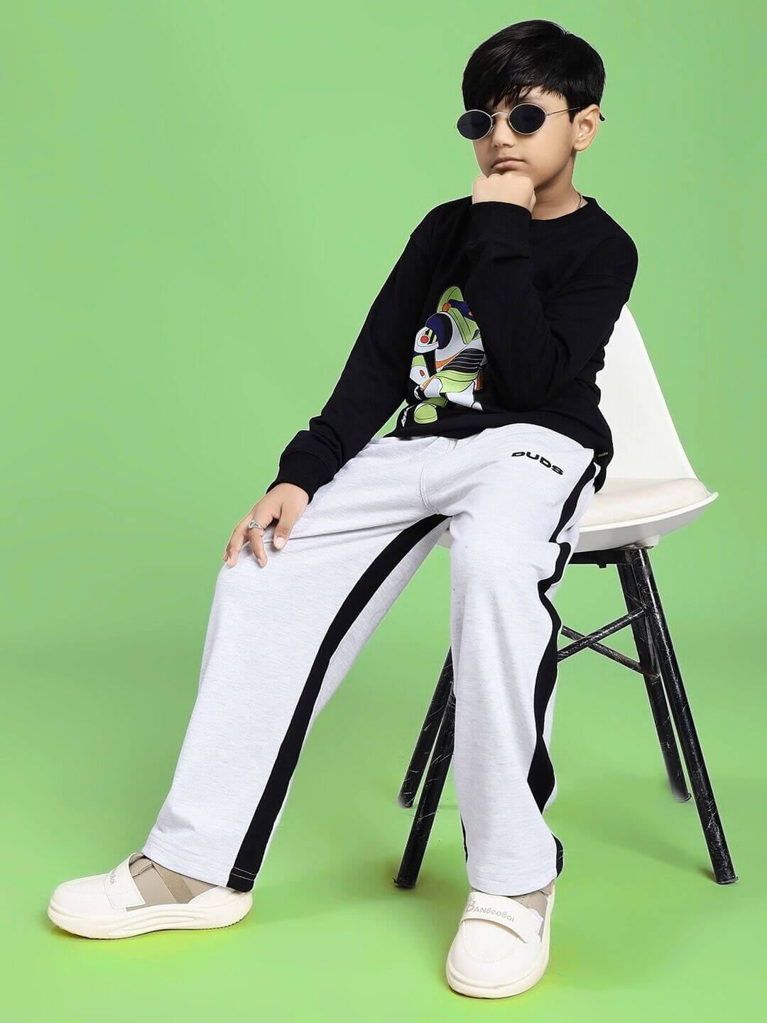 SIDE SEAM BAGGY JOGGER FOR BOYS AND GIRLS GREY BLACK worn by a child sitting on a chair with green background