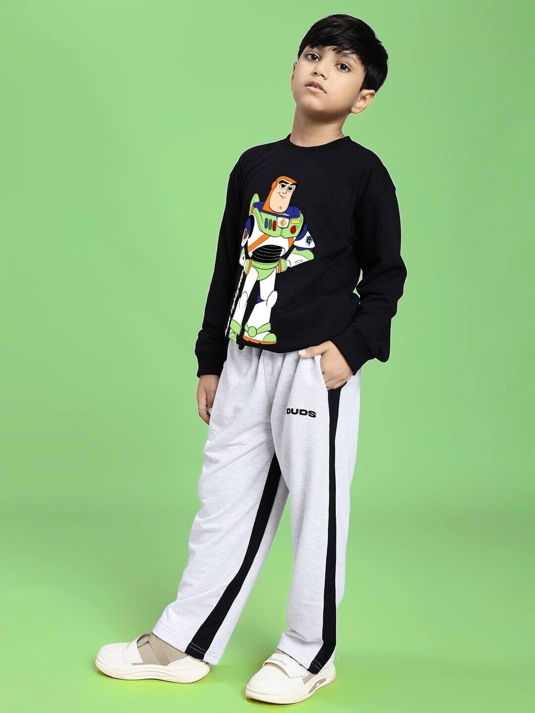 Boy wearing SIDE SEAM BAGGY JOGGER FOR BOYS AND GIRLS GREY BLACK with a colorful sweatshirt on a green background.