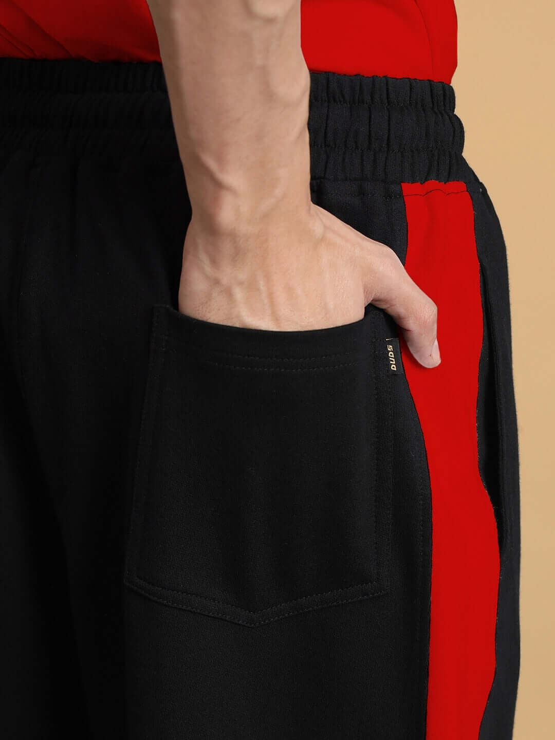 Close-up of side seam baggy joggers in black-red with pocket detail by DUDS, highlighting customizable fit option.