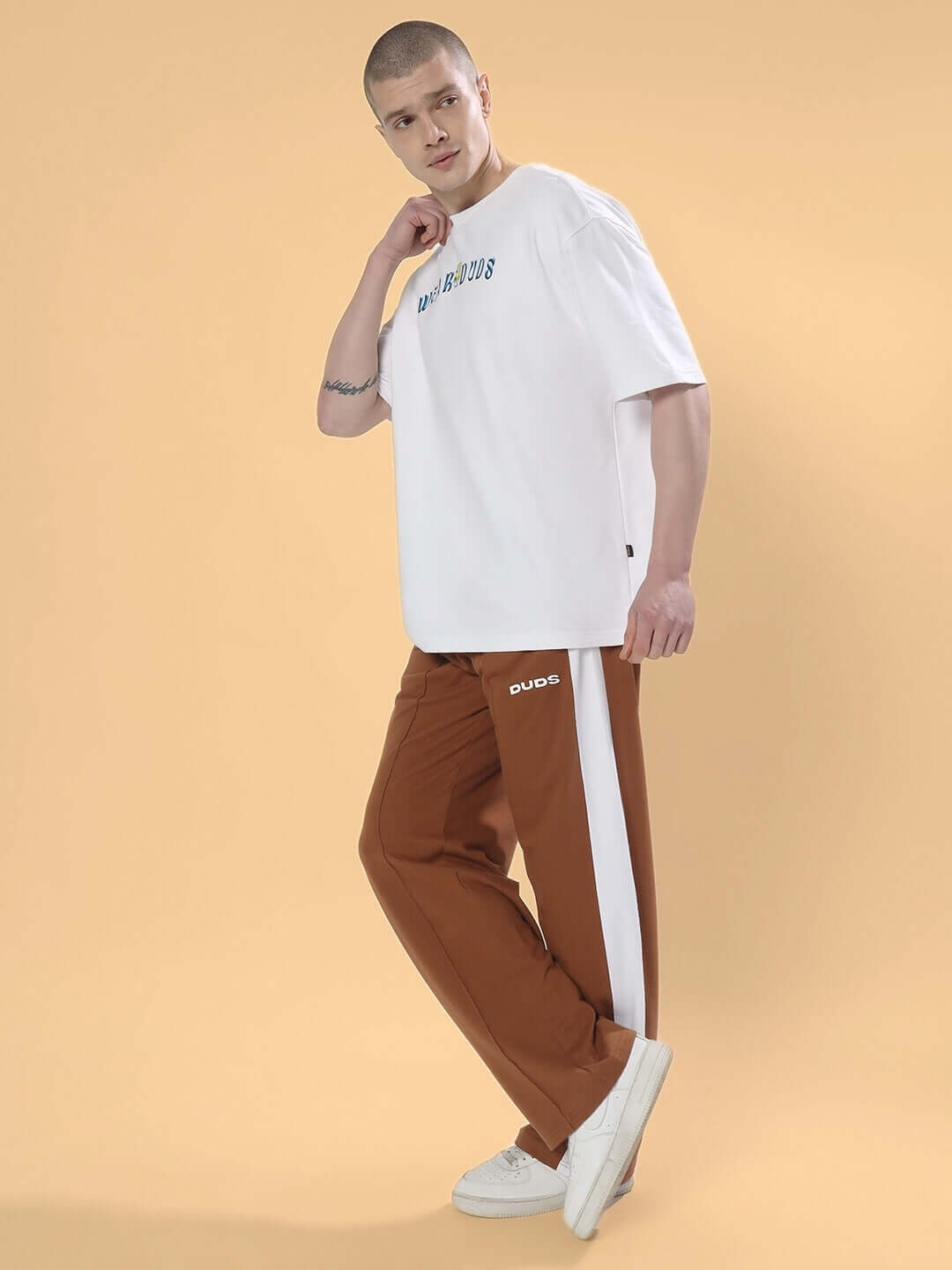 Model wearing brown side seam plated joggers with white stripe, paired with a white T-shirt and sneakers, on a beige background.