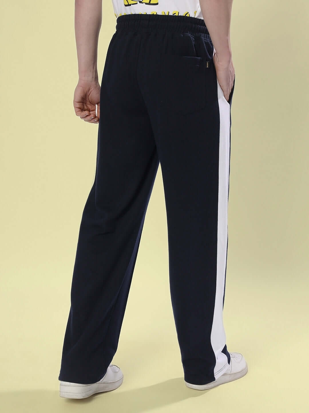 Back view of navy blue side seam plated joggers with white stripe, worn by a model, showcasing casual and comfortable style.