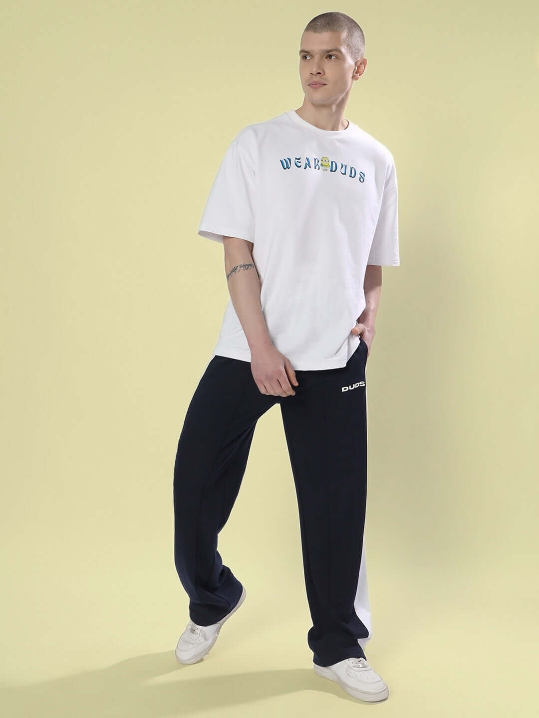 Man wearing navy blue side seam plated joggers with white t-shirt by DUDS, standing on light background.
