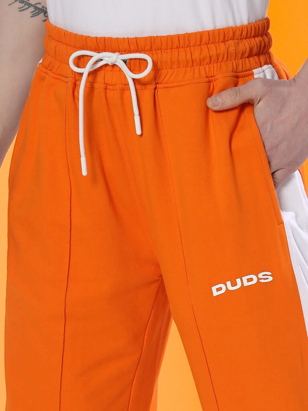 Close-up of orange side seam plated joggers with a drawstring waist and DUDS logo, showcasing tailored fit and detailing.