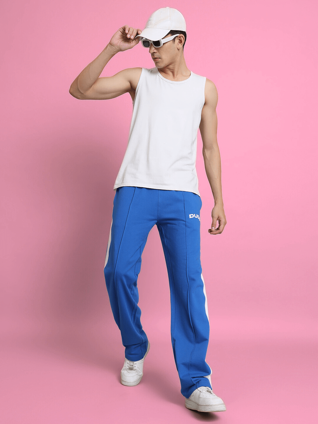 Model wearing SIDE SEAM PLATED JOGGERS in Royal Blue with white tank top and cap, stylish made-to-order joggers by DUDS.