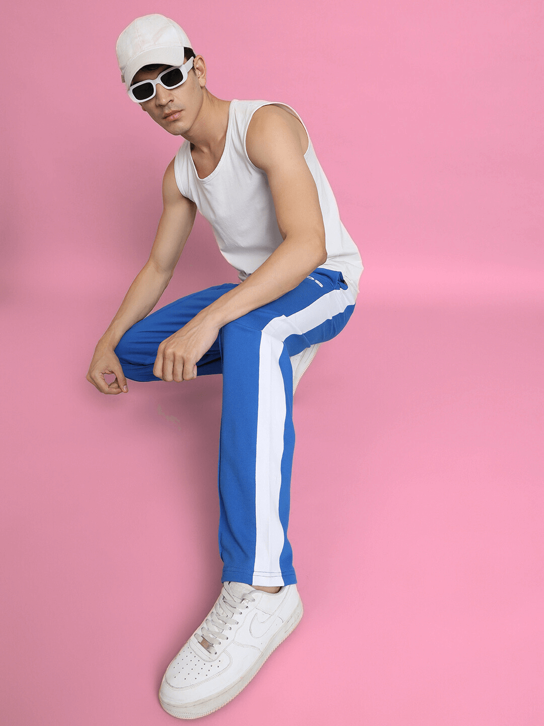 Model wearing SIDE SEAM PLATED JOGGERS in royal blue, sitting with a stylish pose against pink background.