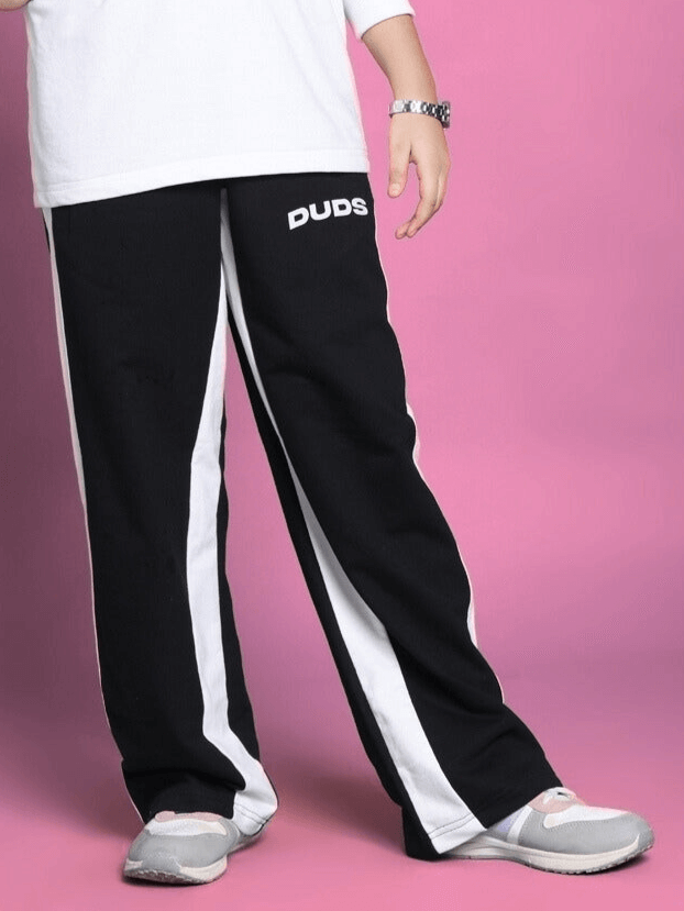 Child wearing DUDS black side seam baggy jogger with white stripes, suitable for boys and girls, against a pink background.