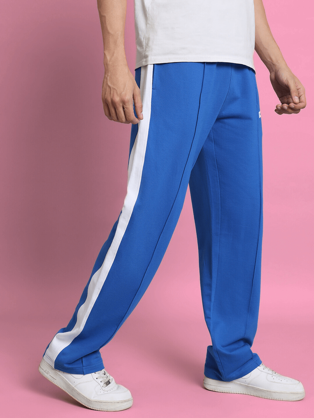 Royal blue side seam plated joggers for men with white stripe detail, styled against a pink background.