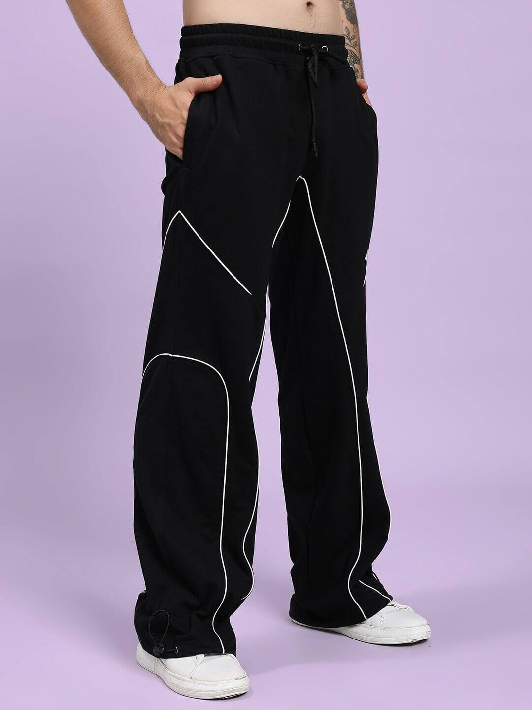 Person wearing SIGNATURE PIPING JOGGERS BLACK with contrast piping, relaxed fit for comfort on a purple background.