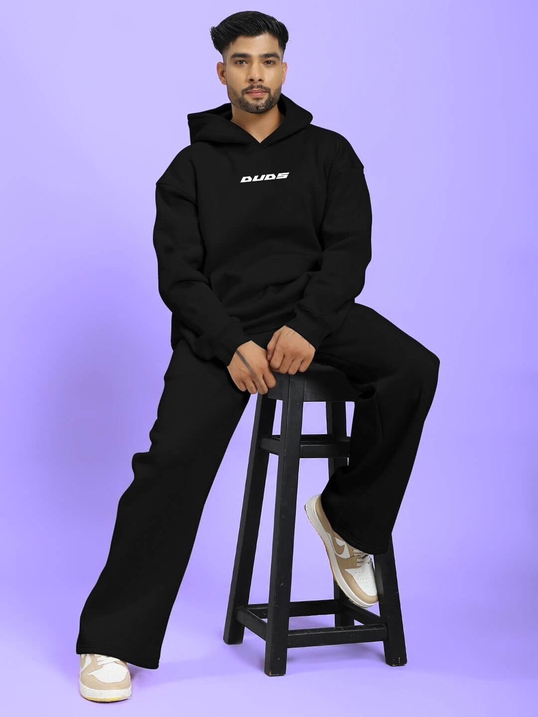 Man wearing SILVER SURFER FLEECE CO-ORD SET BLACK sitting on a stool against a purple background
