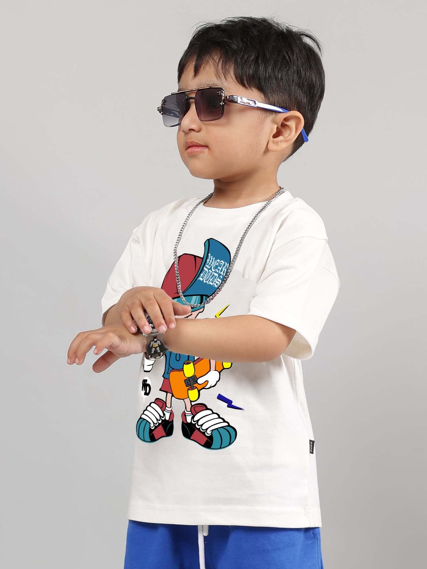 Child wearing off-white SKATE RIDER T-shirt with colorful graphics, sunglasses, blue shorts, and a chain necklace, posing confidently.