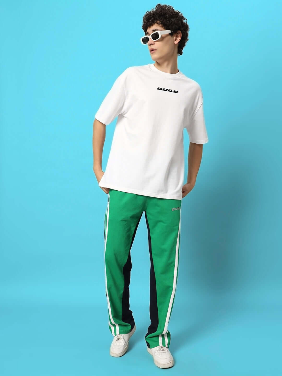 Model wearing Skater Korean Baggy Joggers in green and black by DUDS, paired with a white t-shirt, standing against a blue background.