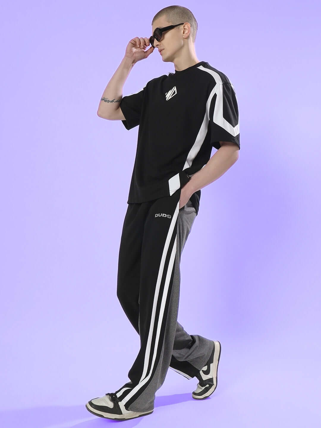 Person wearing DUDS Skater Korean Baggy Joggers in black grey, styled with sporty black t-shirt and sneakers on a purple background