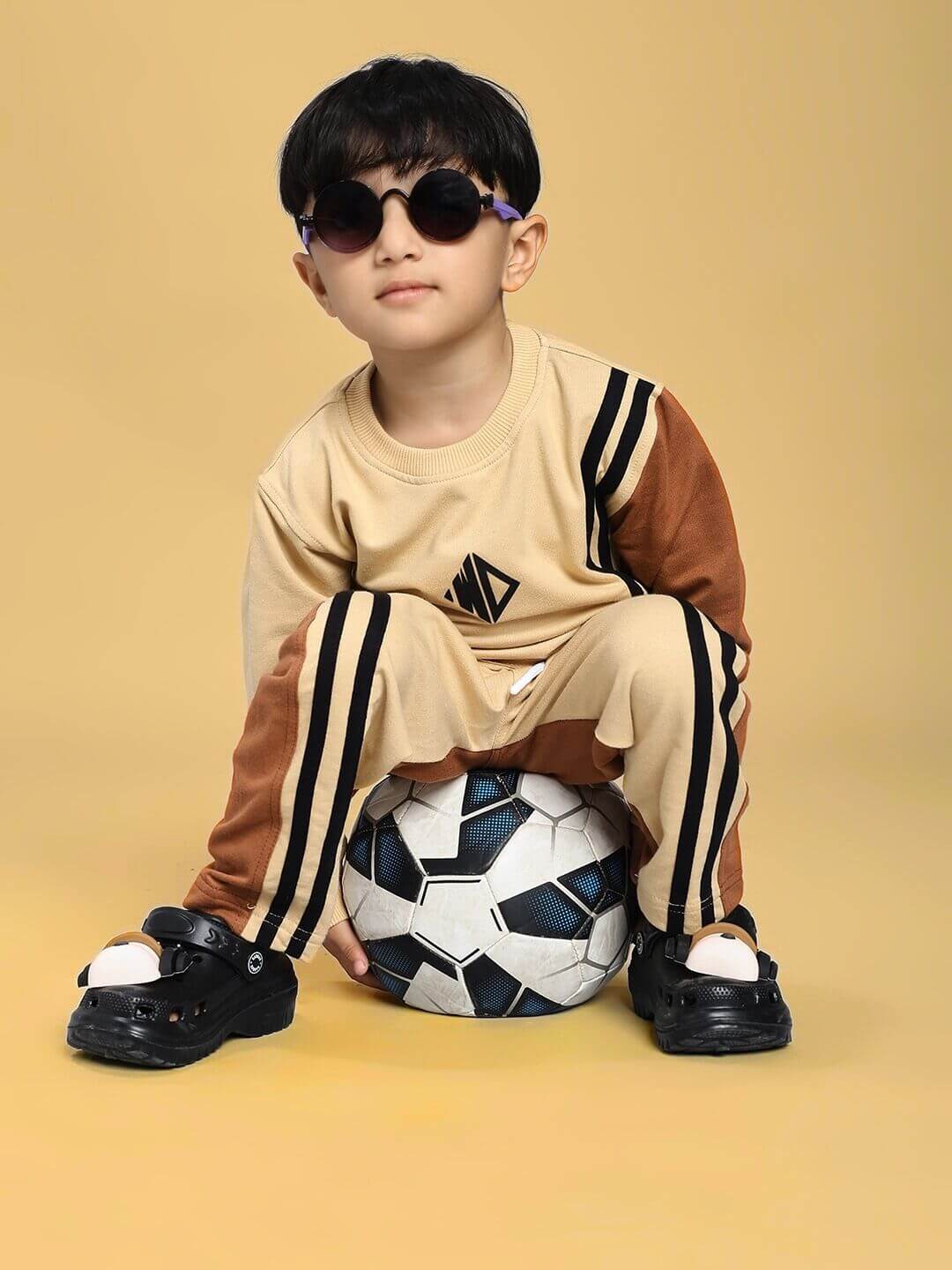 Child wearing SKATER KOREAN CO-ORD FOR BOYS AND GIRLS CREAM BROWN sitting on a soccer ball with sunglasses.