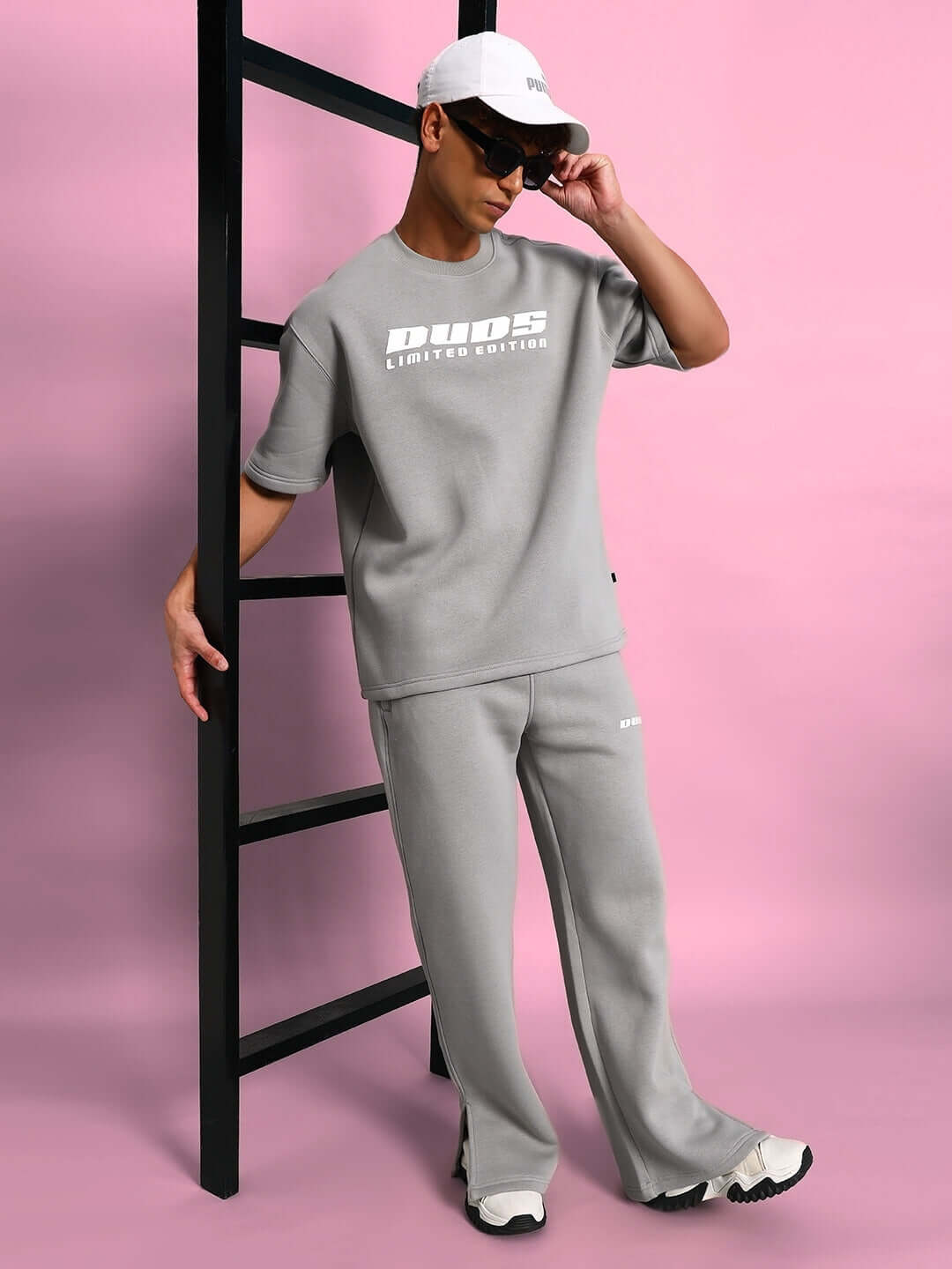 Model wearing SKODA FLEECE OVERSIZED T-SHIRT GREY, showcasing relaxed fit and unisex style against a pink background, paired with accessories.