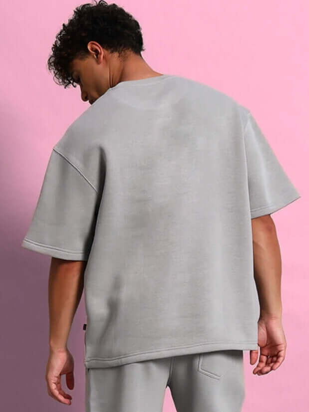 Back view of person wearing SKODA FLEECE OVERSIZED T-SHIRT GREY against a pink background.