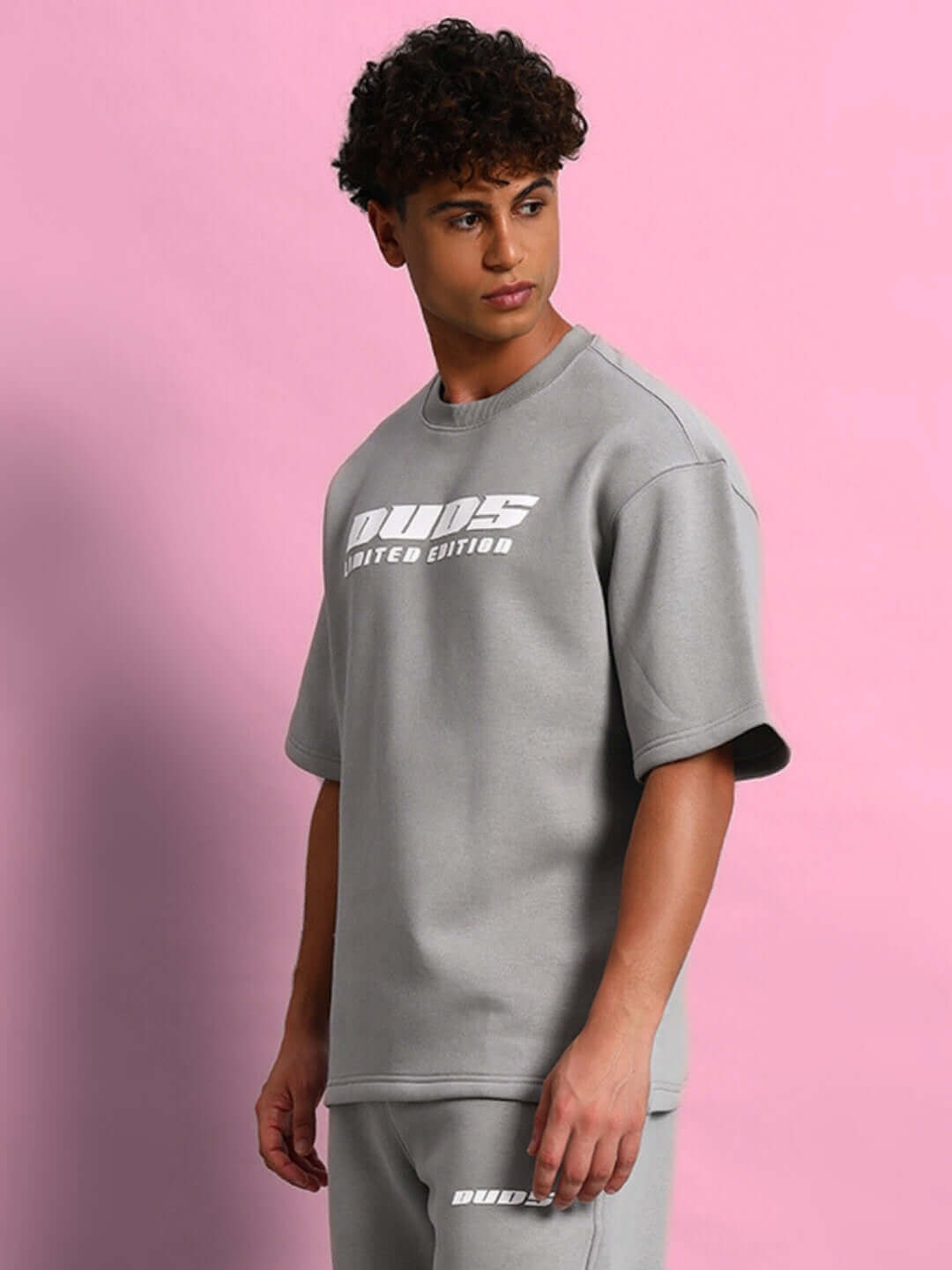 Model wearing SKODA FLEECE OVERSIZED T-SHIRT GREY against pink background, showcasing modern streetwear style and comfort.