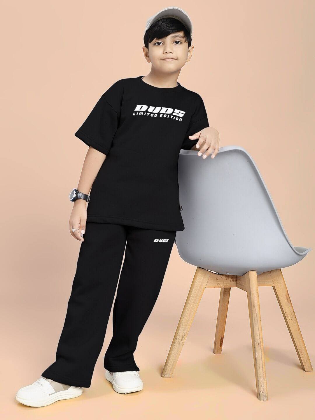 Boy wearing SKODA FLEECE CO-ORD FOR BOYS AND GIRLS BLACK outfit, posing by a chair.