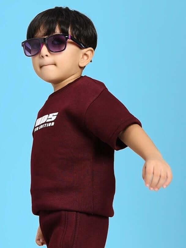 Young child wearing a SKODA FLEECE T-SHIRT FOR BOYS AND GIRLS MAROON, posing with sunglasses against a blue background.