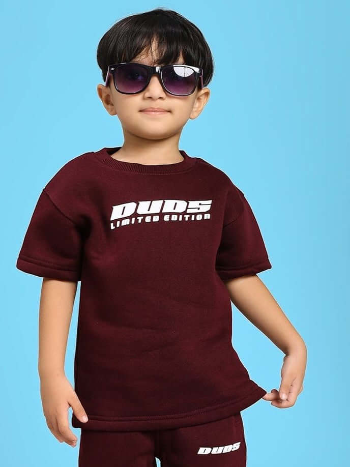 Child wearing SKODA FLEECE T-SHIRT FOR BOYS AND GIRLS MAROON with sunglasses, posing confidently against a blue background.