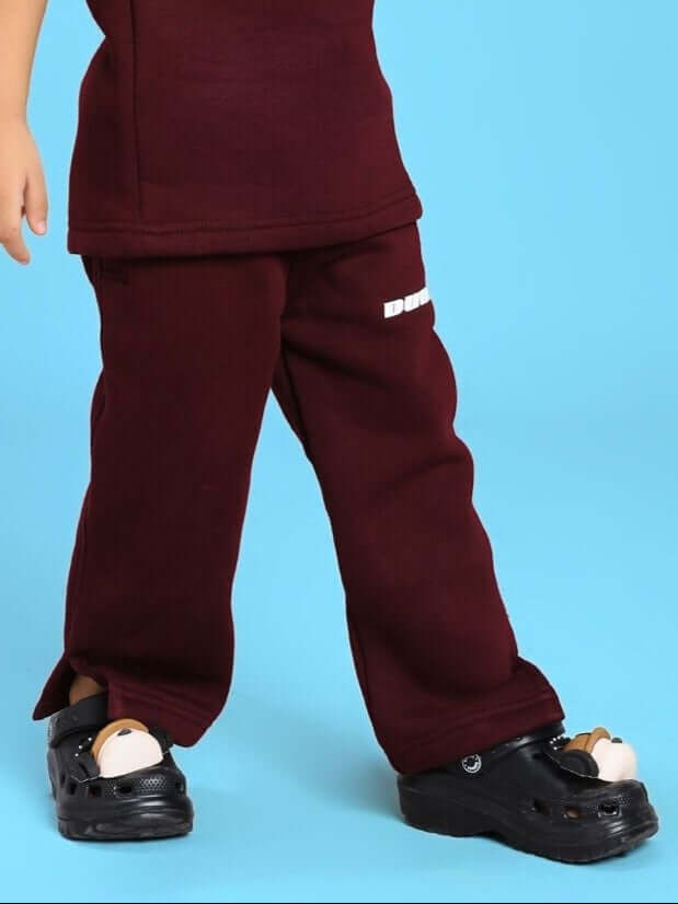 Child wearing SKODA FLEECE JOGGER FOR BOYS AND GIRLS MAROON with black shoes on blue background