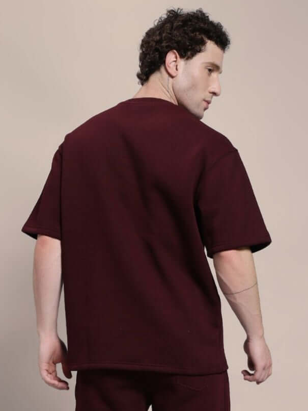 Man wearing SKODA FLEECE OVERSIZED T-SHIRT MAROON, showcasing back view, highlighting soft fleece fabric and casual style.