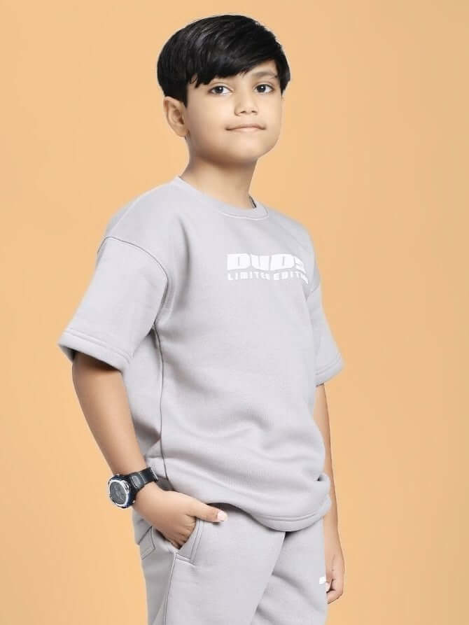 Boy wearing SKODA FLEECE T-SHIRT FOR BOYS AND GIRLS GREY with watch against peach background.