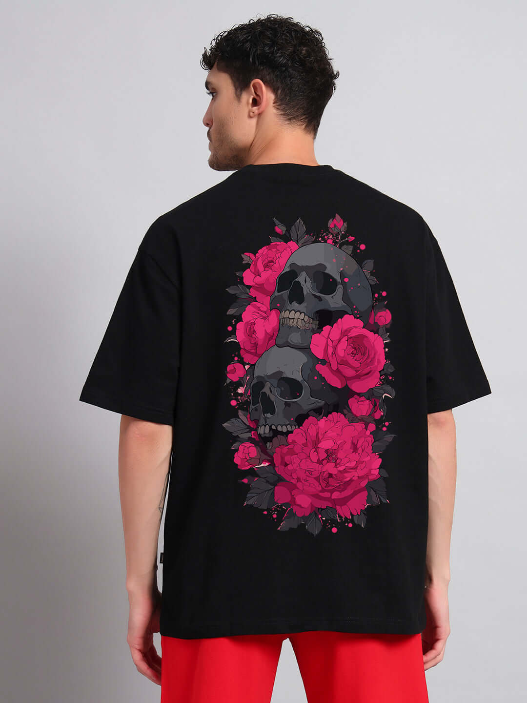 Man wearing SKULL ROSES OVERSIZED T-SHIRT BLACK featuring skulls and roses graphic on the back.