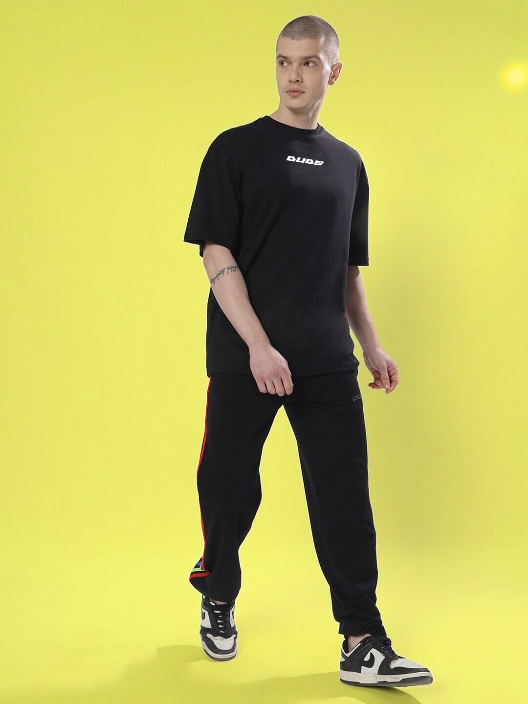 Person wearing a black SKULL CYBERPUNK OVERSIZED T-SHIRT BLACK, standing against a bright yellow background.