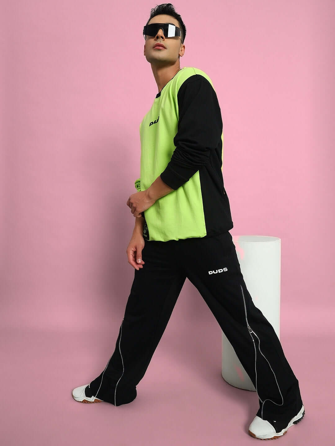Model wearing black slider joggers by DUDS, showcasing modern fit and style, set against a pink background.