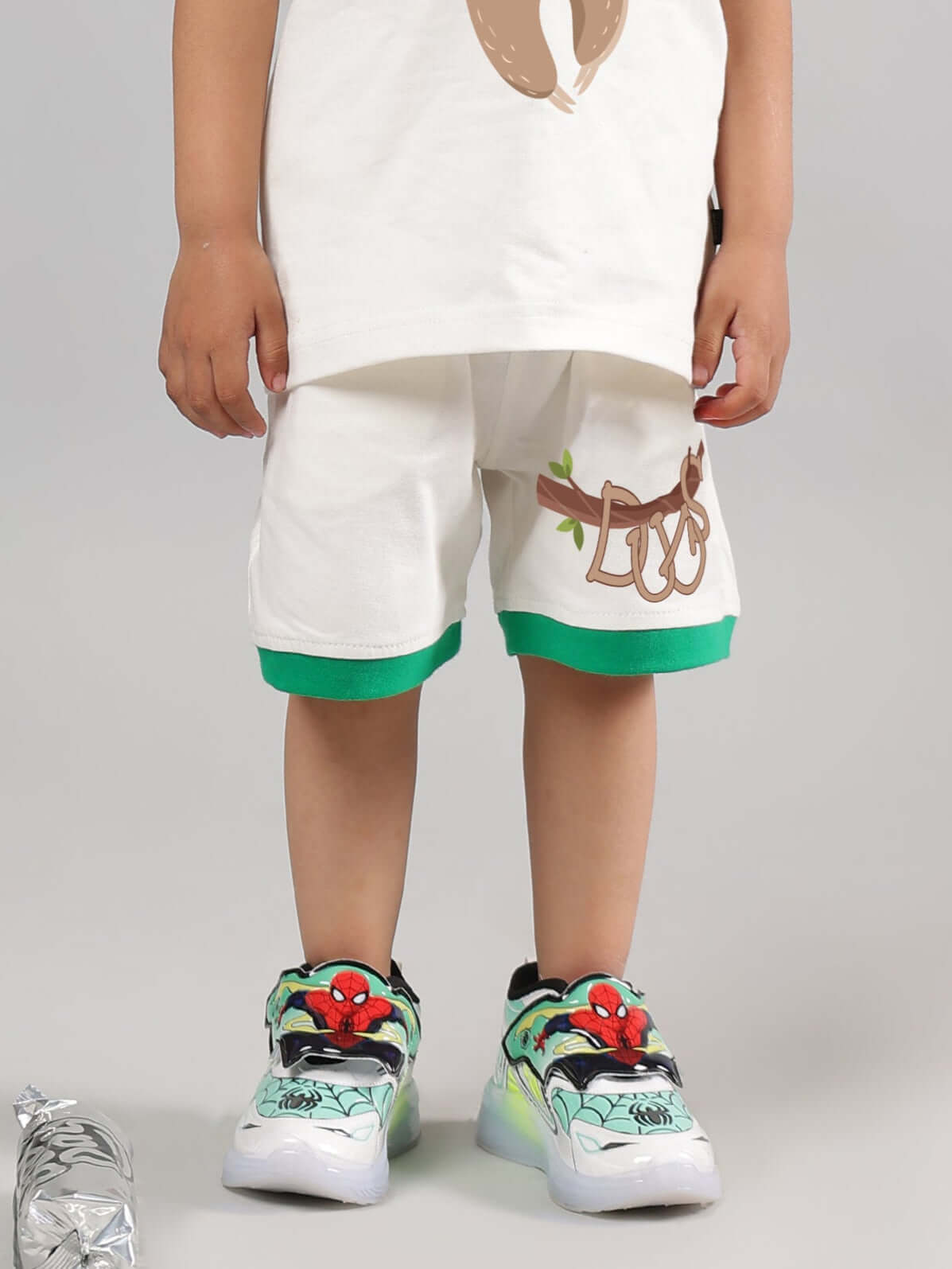 Off-white sloth shorts for kids, with green trim, shown on a child; designed by DUDS. Perfect for custom fit and made-to-order options.