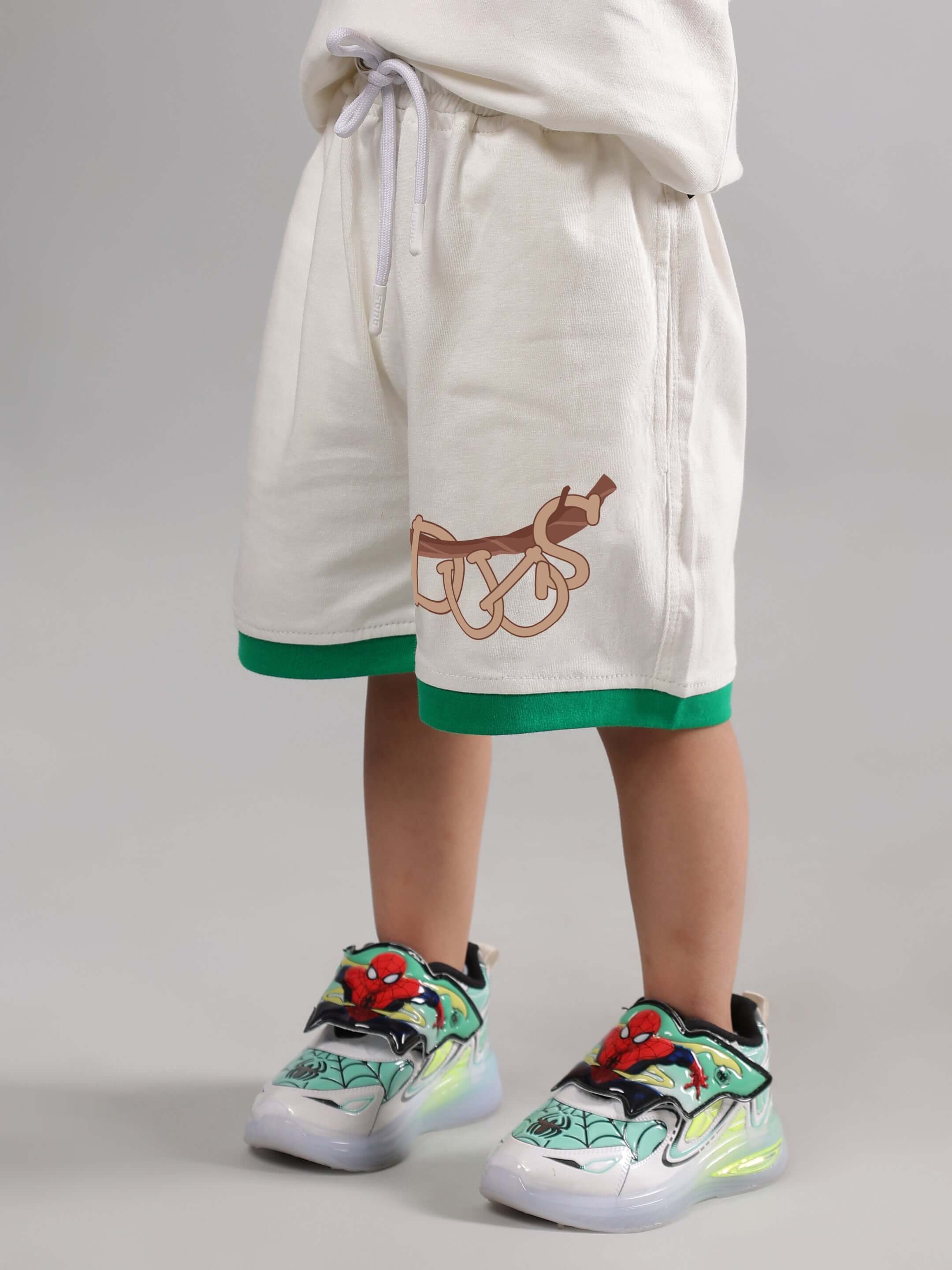 Boy wearing off-white sloth shorts with green trim, illustrated logo, and colorful sneakers.